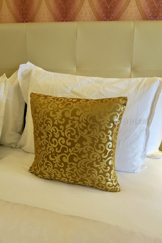 豪华的特大号床，金色的散垫和白色的枕头/折叠的床单，奶油色的高皮革钉床头板靠墙，家庭家具和卧室室内设计有金色的靠垫和百合花图案设计